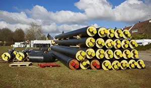 Stacked district heating pipes and district heating lines with yellow ends lie piled up in a meadow