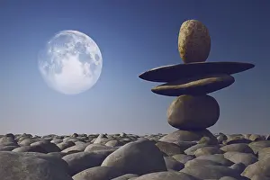 Stacked stones in sunlight with moon in sky on pebble sea beach