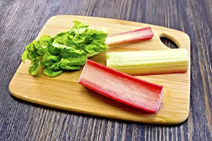 The stalks of rhubarb with green leaf on the planch on a dark wooden board