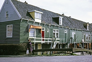 Standing woman posing for cameras next to traditional village houses, Marche, Netherlands, 1973
