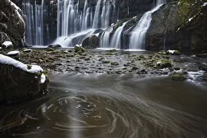 Steady waterfall flows over moss-covered stones in a calm river