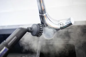 A steam brush cleaning around a chrome kitchen faucet