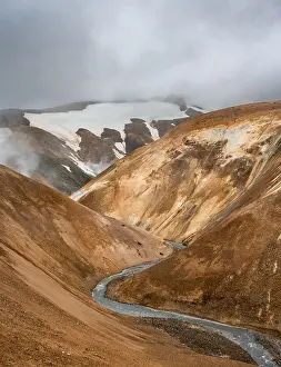Steaming stream between colourful rhyolite mountains with snowfields