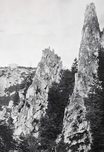Steep and high rocks protrude from a wooded area
