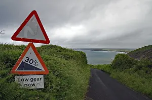 A steep road sign stands out against a dramatic coastal landscape