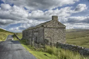 Stone barn, dry stone walls and sheep standing on the road