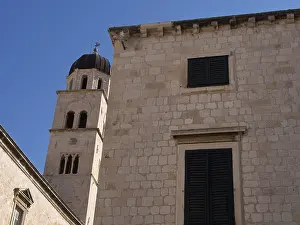 Stone building with shutters and bell tower in the background