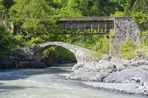 Stone and car bridge crossing a river in a mountainous forest landscape