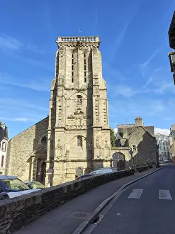 A stone church tower rises at the end of an urban road