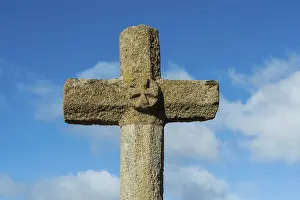 Stone cross stands tall against a bright blue sky with scattered white clouds in the background