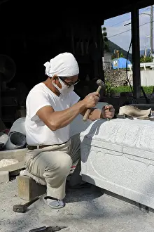 Stonemason chiseling at the base of a stone lamp