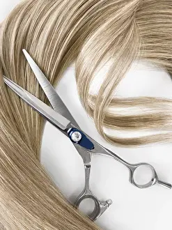 A strand of blond hair with scissors on a white background