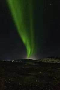 Stream of green aurora lights arcs across a starry night over the coastline