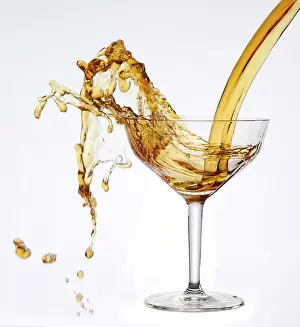 A strong flood of golden yellow liquid pours into a cocktail glass and spills over