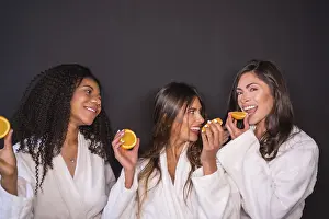 Studio photo with grey background of multi-ethnic relaxed women in bathrobe eating fruit