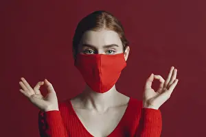 Studio portrait of young woman in protective medical face mask isolated on red background