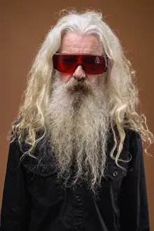 Studio shot of senior bearded man wearing black shirt against brown background