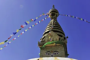 A stupa with colourful prayer flags in front of a clear blue sky