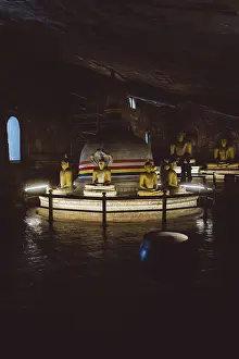 A stupa surrounded by Buddha statues in a dimly lit temple room