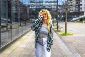 Stylish young woman with blond curly hair and sunglasses dances in a modern urban setting