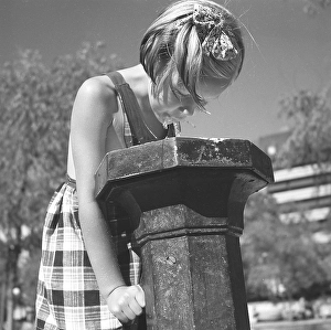 Summer of the 1940s. A young girl in a summer dress drinks from a water fountain in one of Stockholms parks