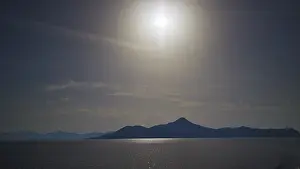 Sun over a mountain silhouetted against a calm sea