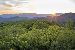 Sun rays emerging over a lush, green mountain range at sunset creating a peaceful scene
