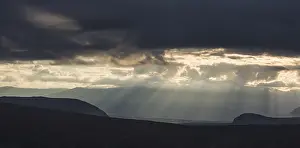Sun rays fall through clouds in mountain landscape