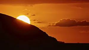 Sun setting behind a mountain, clear silhouette in front of an intense orange sky