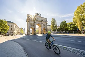 Sun star, Siegestor, cyclist riding along Leopoldstrasse