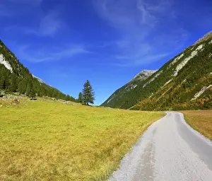 Sunny autumn day. Wide dirt road in an Alpine valley