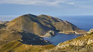 Sunny coastal road winding along a mountainous landscape overlooking the sea