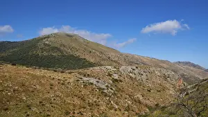 Sunny sky over a barren mountain landscape with green vegetation