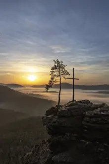 Sunrise with fog, peak with cross and tree on a sandstone rock