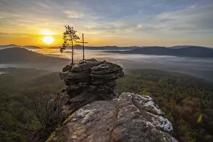 Sunrise on a rock with a summit cross and a view over a forest