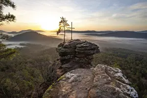 Sunrise on a rock with a summit cross and a view over a forest
