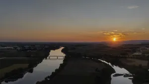 Sunset over a calm river with railway bridge and surrounding landscape