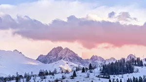 Sunset with dramatic sky and snowy mountain peaks illuminated by sunlight