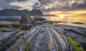 Sunset at the sea, in front rocky coast with grass and lichens