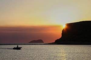 Sunset, sun behind mountain, boat as silhouette
