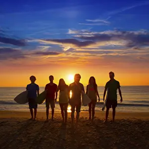 Surfers teen boys and girls group walking on beach at sunshine sunset backlight