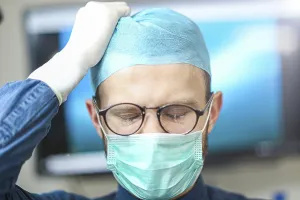 A surgeon adjusting his cap, appearing concentrated and careful