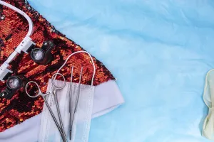 Surgical tools and a medical mask on red sequins against a blue backdrop