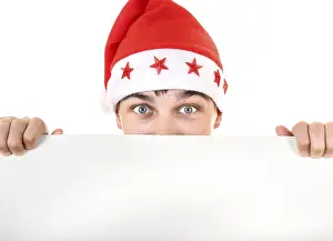 Surprised Teenager in Santa's Hat behind Empty White Board Closeup Isolated On The White Background<br> Surprised