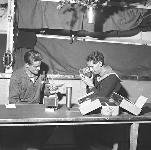 Swedish sailors in the Swedish navy in 1942. One of the sailors is holding up a model of a sailing ship that looks only just begun, while the other is filming with a film camera