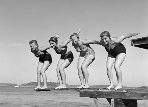 Swimming in the 1940s. A line of four women are standing ready to jump in the water on a summer's day