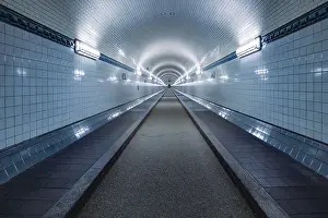 A symmetrical tunnel with white tiles and lighting stretches into the distance