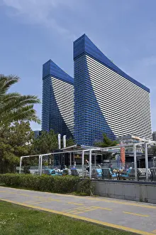 Two tall blue buildings with modern architectural features and a terrace in an urban environment