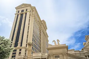 Tall building showcasing classic roman architectural design with columns and horse statues under a bright blue sky
