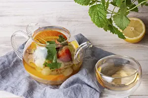 Tea with fruits and berries in a glass teapot on a white wooden background